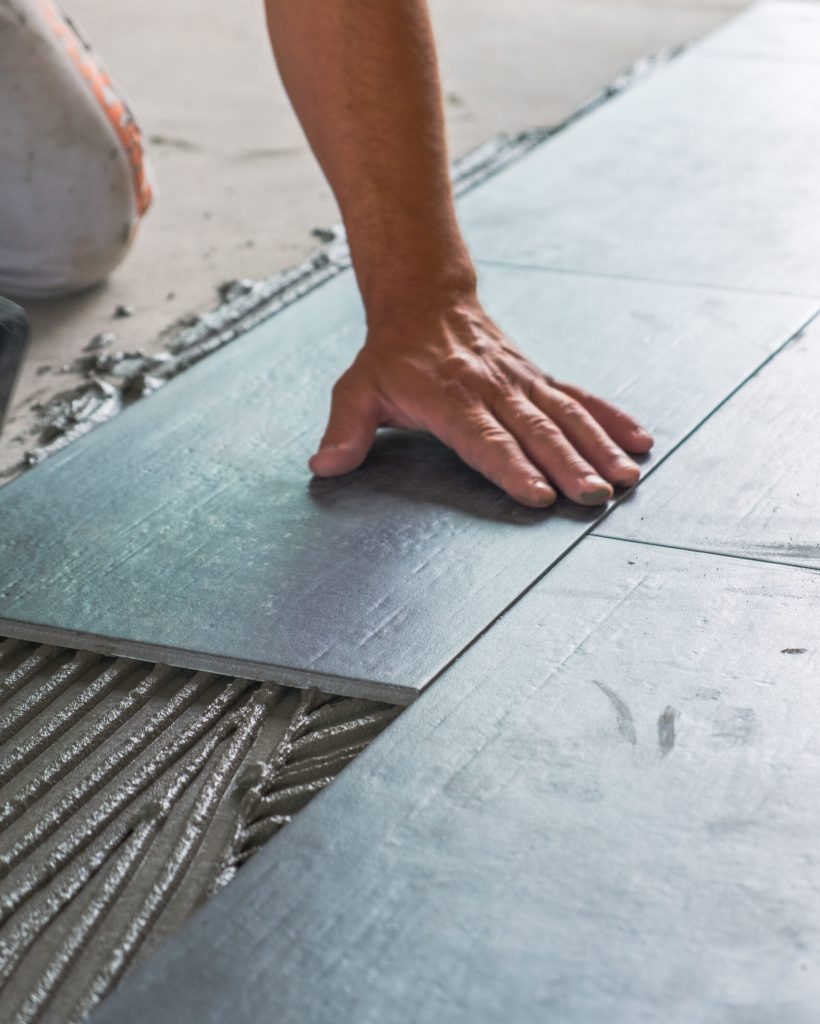 Worker’s hands pressing ceramic floor tiles laid on applied adhesive Worker's hands pressing ceramic floor tiles laid on applied adhesive
